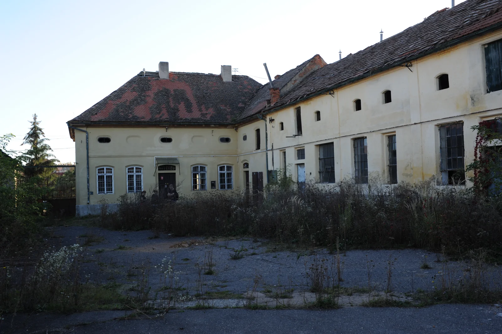 Zanedbaný dvůr se zarostlou plochou a původními hospodářskými budovami