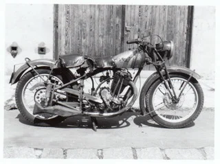 Motocykl Plicka před dřevěnými vraty
